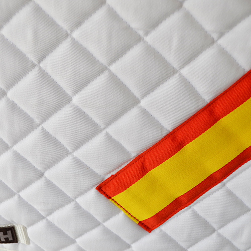 tecido branco acolchoado com etiqueta vermelha e amarela e etiqueta com letra H