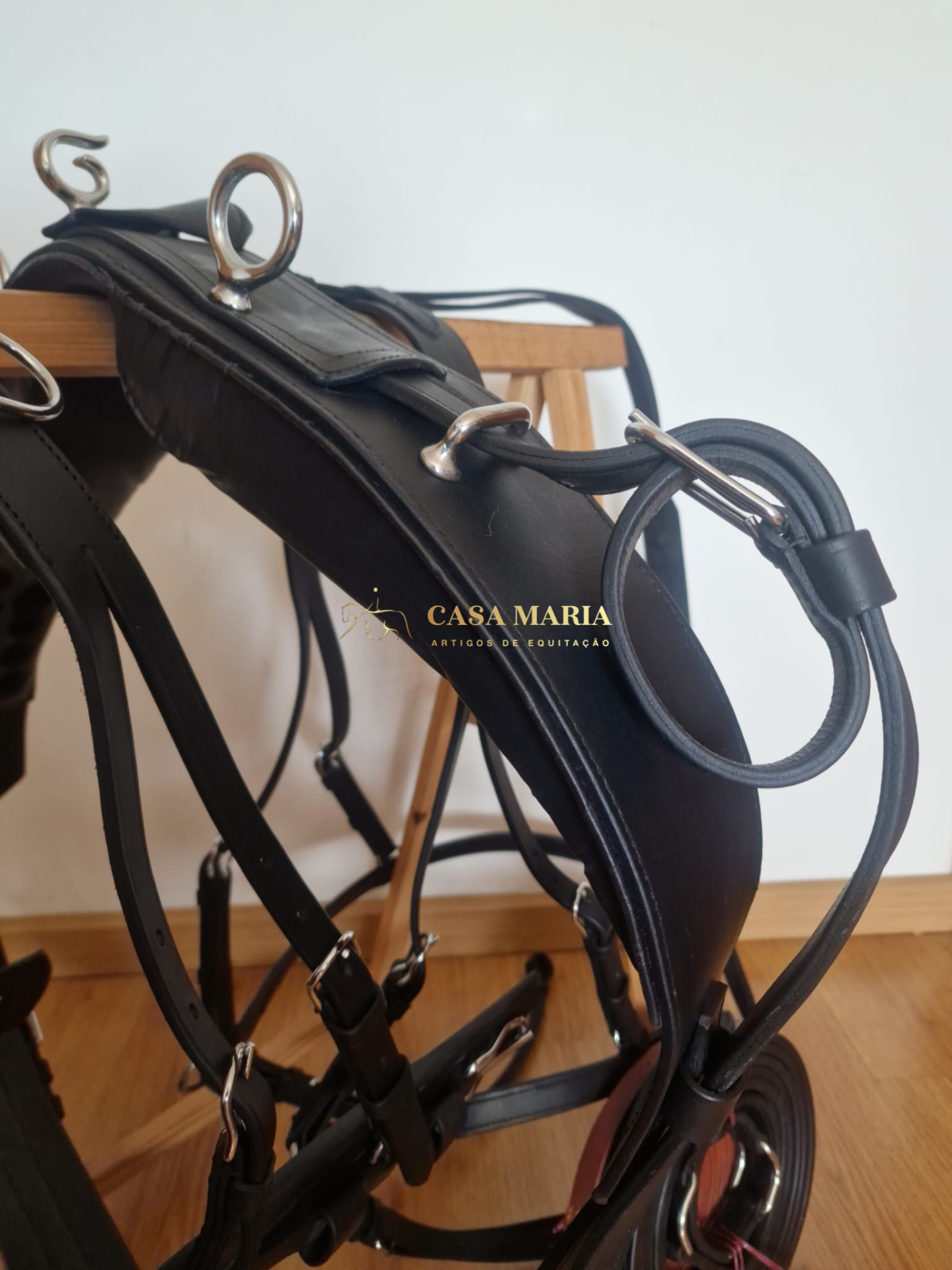 Peça de arreio em couro preto com ferragens metálicas e logotipo CASA MARIA