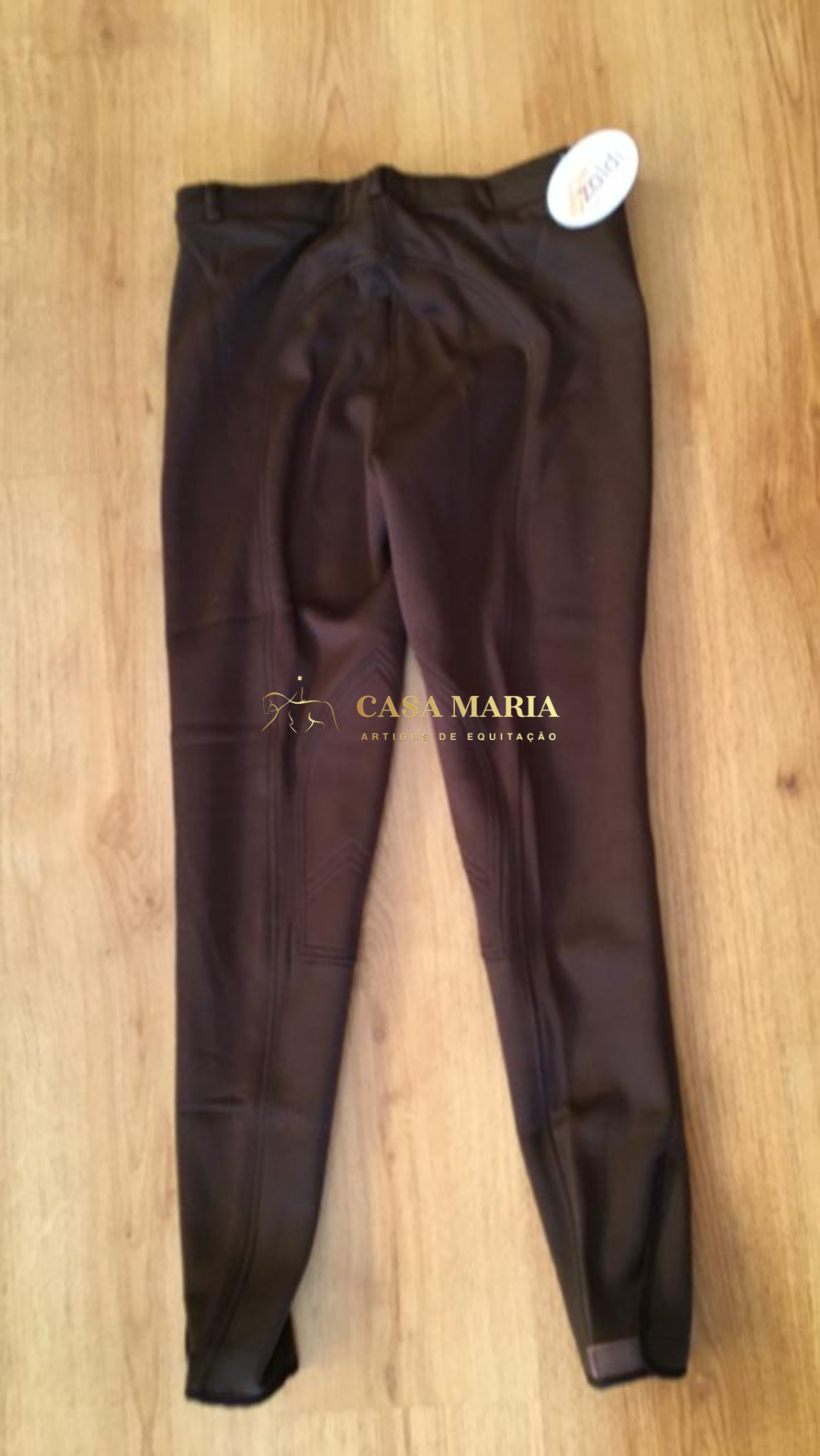 Calças castanhas escuras de equitação com etiquetas sobre chão de madeira