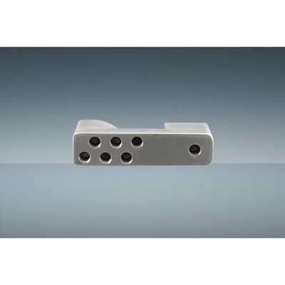 Peça metálica cinzenta com vários orifícios sobre superfície espelhada