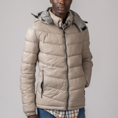 Casaco acolchoado bege com fecho de correr preto, usado por homem com camisa aos quadrados e jeans azul