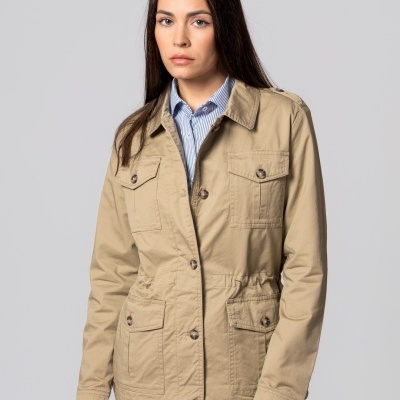 Casaco bege claro com botões e bolsos, mulher com camisa riscada e jeans, fundo cinza claro