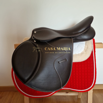 Sela negra de couro sobre manta branca e vermelha num suporte de madeira