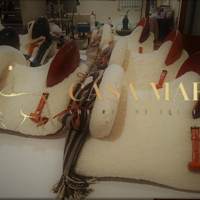 Almofadas brancas com couro castanho e tecidos rústicos em oficina com texto CASA MARIA