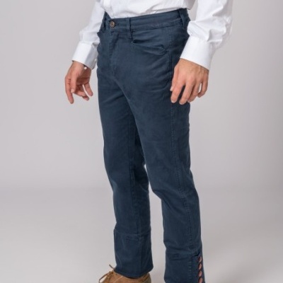 Calças azuis escuras de homem com detalhes vermelhos na bainha, camisa branca e sapatos castanhos em fundo cinzento