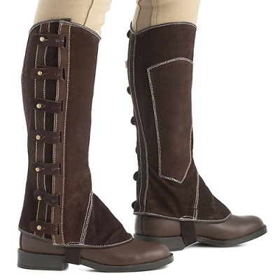 Perneiras de equitação castanhas com correias laterais usadas com calças claras.