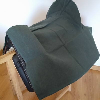 Sela de equitação preta coberta com tecido verde escuro sobre suporte de madeira