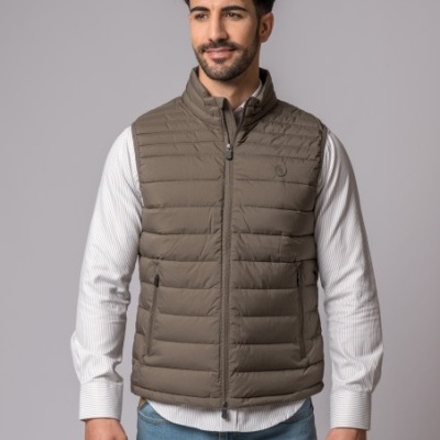 Colete acolchoado castanho claro em homem com camisa branca e calças de ganga, fundo cinza.