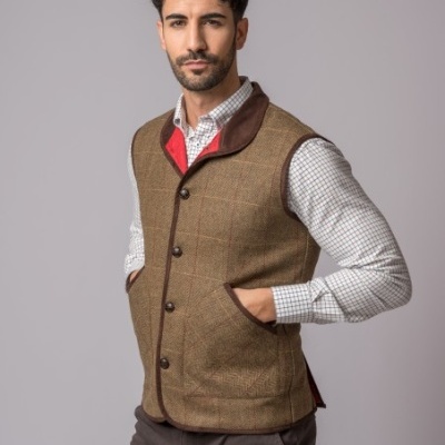 Homem com colete castanho xadrez, camisa branca xadrez e calças castanhas