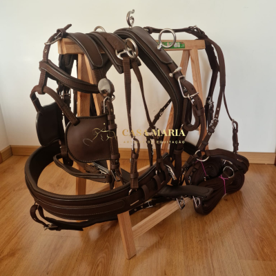 Arnês de equitação em couro castanho com fivelas metálicas prateadas sobre suporte de madeira