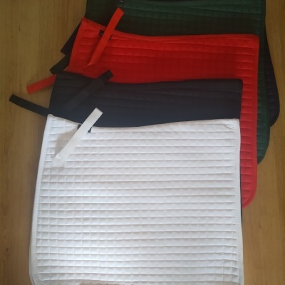 Cinco mantas de sela acolchoadas em várias cores, dispostas sobre fundo de madeira