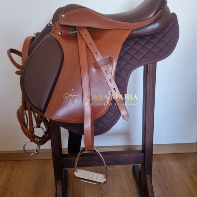 Sela de equitação em pele castanha sobre almofada matelassada castanha numa estrutura de madeira.