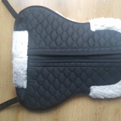 Suporte para sela de cavalo acolchoado preto com bordas brancas felpudas sobre madeira clara