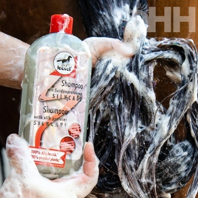 Frasco de champô transparente com tampa vermelha em mãos ensaboadas com cabelo molhado e ensaboado ao fundo