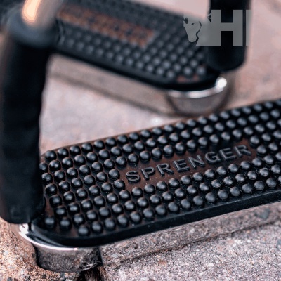 Estribos metálicos com apoio de borracha texturizada preta e texto SPRNGER sobre piso de pedra