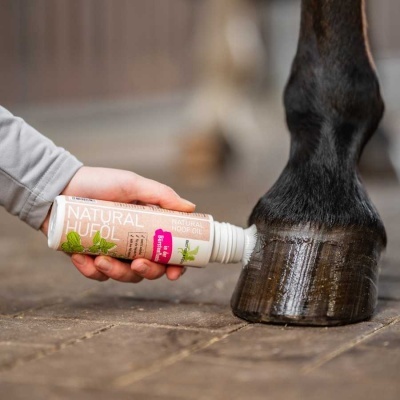 Tubo NATURAL HUFOL sendo aplicado no casco de cavalo preto sobre chão de pedra