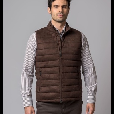 Homem com colete castanho acolchoado e camisa de riscas em fundo cinzento