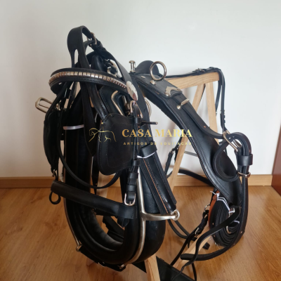 Arnês e rédeas de couro preto com metal prateado pendurados num suporte de madeira