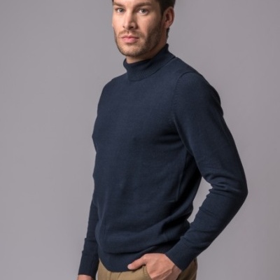 Homem com camisola de gola alta azul escuro e calças castanhas