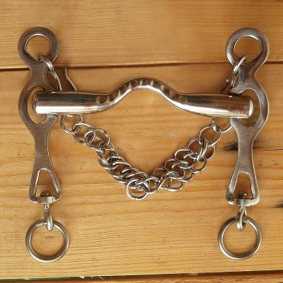 Freio de equitação metal prateado com corrente sobre madeira