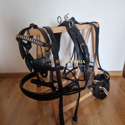 Arreio de couro preto com fivelas metálicas pendurado num cabide de madeira