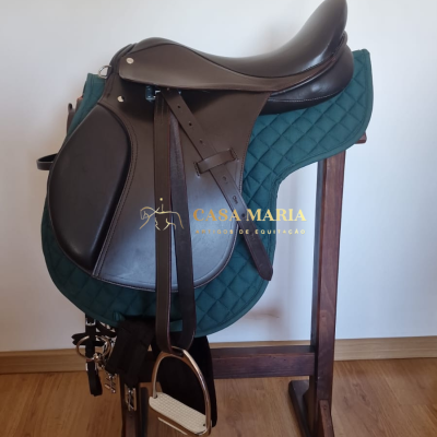 Sela de equitação castanha com alforges e estribos num suporte de madeira