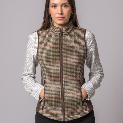 Colete xadrez castanho bege e vermelho com gola alta e fecho de correr, usado por mulher com camisa branca quadriculada e calças pretas.