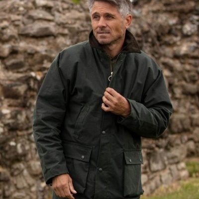 Homem com casaco impermeável verde escuro com gola castanha e bolsos à frente em cenário exterior com muro de pedra