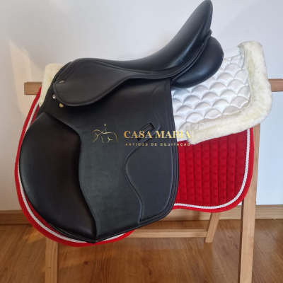 Sela de equitação preta em couro com mantas branca e vermelha sobre suporte de madeira