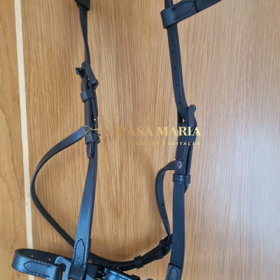 Cabresto de pele preta para equitação com fivelas, suspendido contra fundo de madeira clara