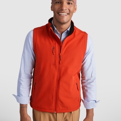 Homem com colete vermelho sobre camisa azul clara e calças beges