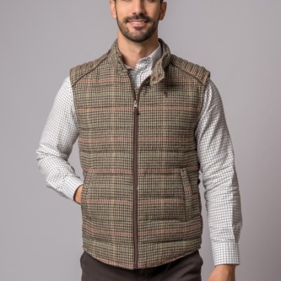 Homem com colete xadrez castanho e camisa branca com padrão posando