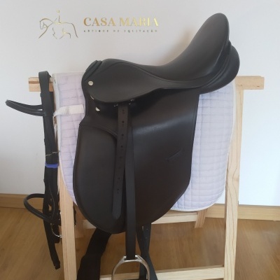 Sela de equitação preta em couro sobre almofada branca e suporte de madeira com cabeçada ao lado