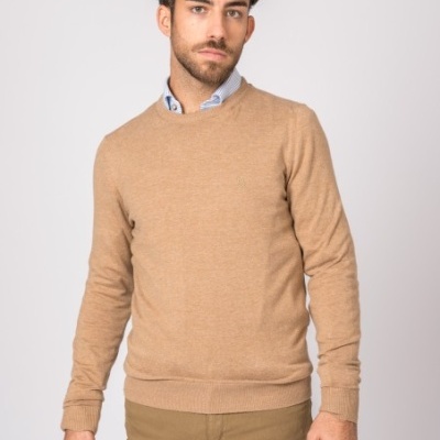 Homem com camisola bege de malha e calças cáqui, camisa azul clara, fundo branco.