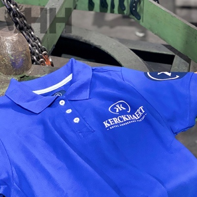 Polo azul com logotipo branco KERCKHAERT sobre superfície metálica verde