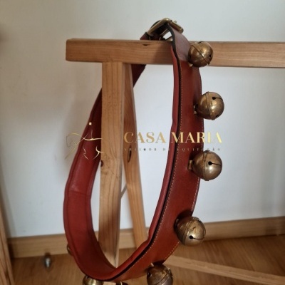 Colar de couro castanho com sinos dourados pendurados na madeira