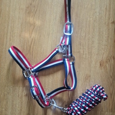 Cabresto e guia para cavalo em tecido com cores vermelho, branco e azul sobre chão de madeira