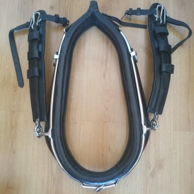 Arreio de cavalo preto almofadado com correias e fivelas num chão de madeira.