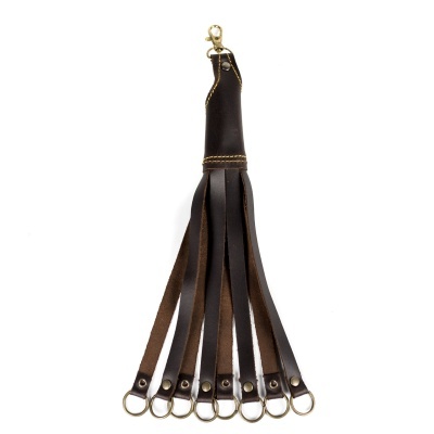 Fusta em couro castanho com várias tiras e argolas metálicas douradas.