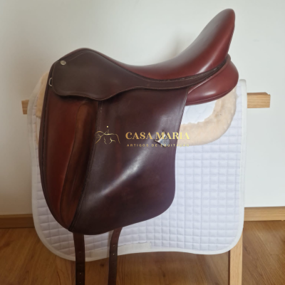 Sela de equitação em pele castanha sobre almofada branca em suporte de madeira