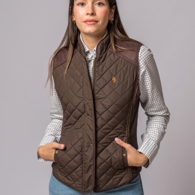 Colete feminino matelassê castanho com detalhes nos ombros e camisa branca com padrões, em fundo cinzento.