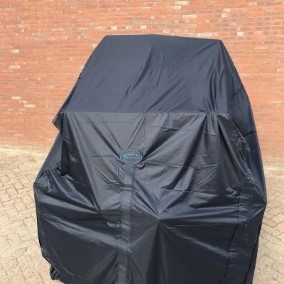 Capa preta de proteção para grelhador com logótipo STEELPRO, junto a uma parede de tijolo vermelho