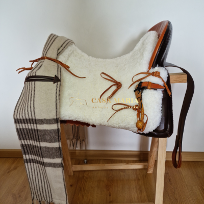 Sela de equitação em couro castanho com almofada branca felpuda e manta castanha e bege pendurada