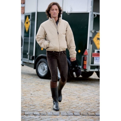 Homem com casaco bege, calças pretas e botas bicolores segurando capacete junto a carrinha.