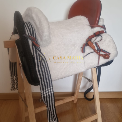 Sela de equitação com materiais em couro castanho e enchimento branco sobre suporte de madeira.