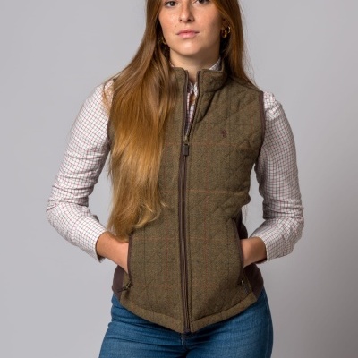 Mulher com colete acolchoado castanho, camisa xadrez branca e calças de ganga azuis