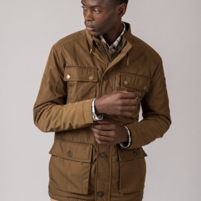 Homem a usar casaco castanho de tecido com bolsos e botões, camisa xadrez e calças bege