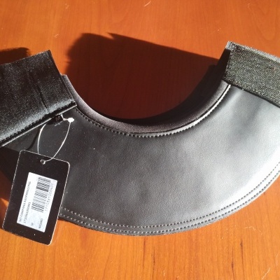 Proteção de ombros cinza com fechos de velcro pretos e etiqueta preta sobre mesa de madeira clara