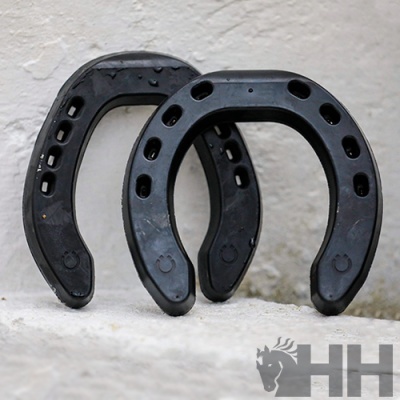 Duas ferraduras pretas de material sintético com orifícios apoiadas numa superfície de cimento branca, com logotipo HH