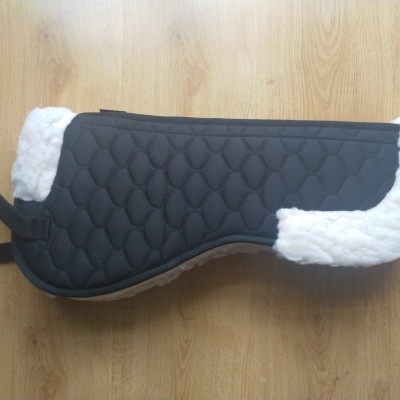 Protector de sela preto acolchoado com bordas brancas felpudas sobre chão de madeira